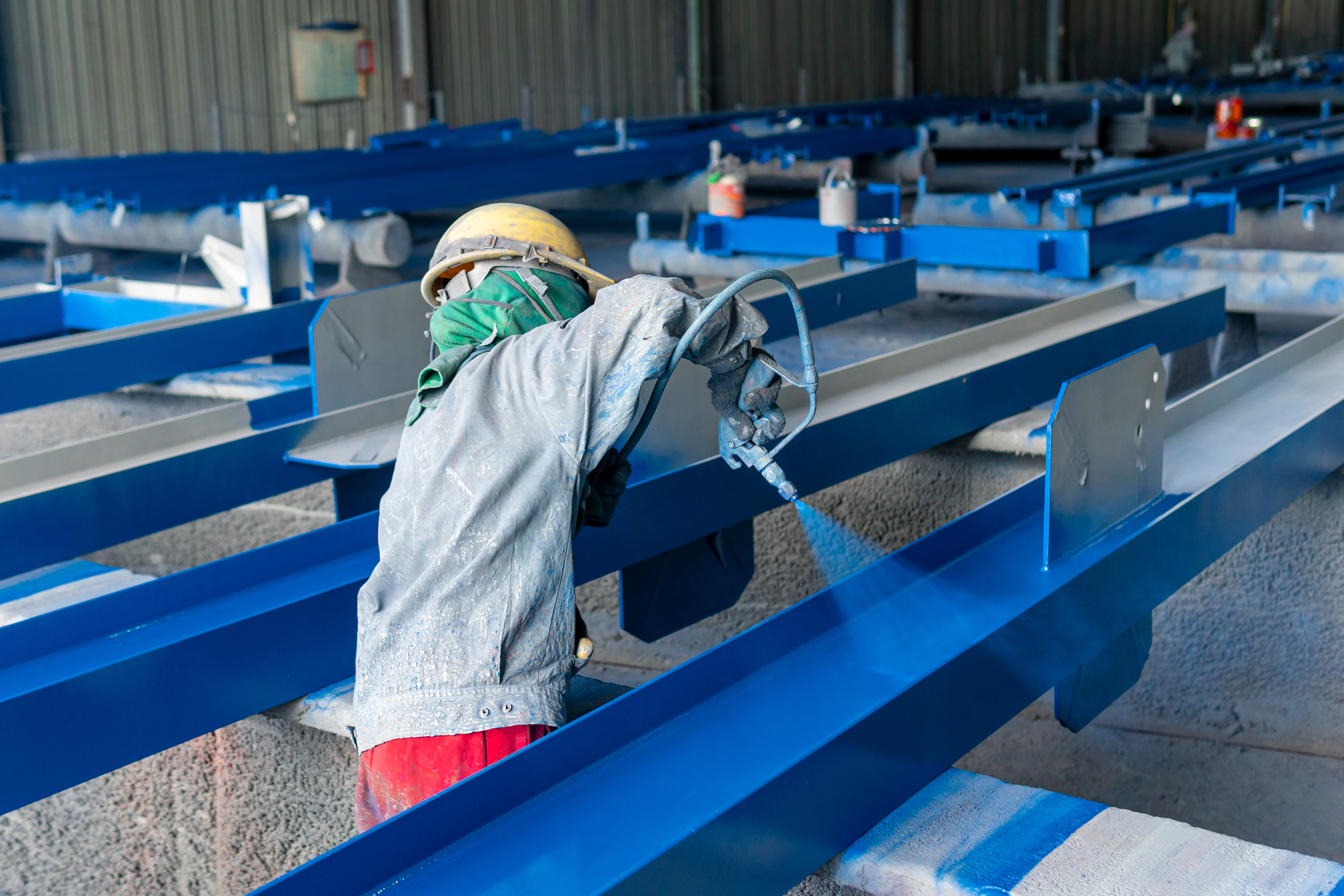 Steel fabricator spray-painting beams